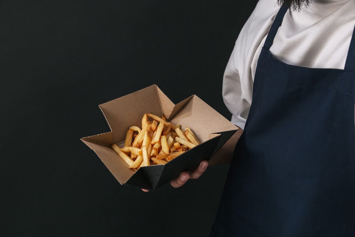 Caja de papas lista para llevar en manos de un mesero