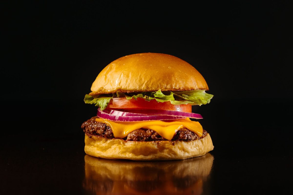 Hamburguesa clásica con queso cheddar, tomate y cebolla morada sobre fondo oscuro