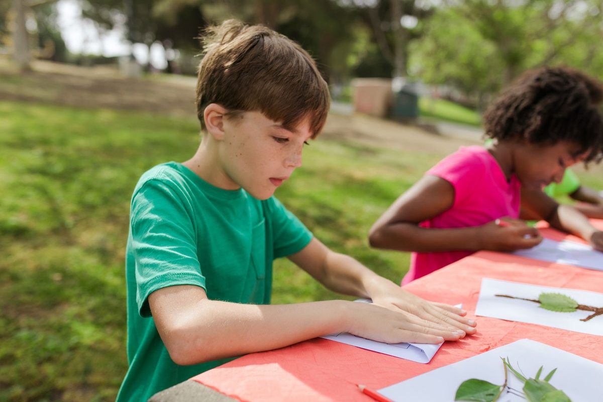 Niños haciendo manualidades en una mesa al aire libre, sobre el césped