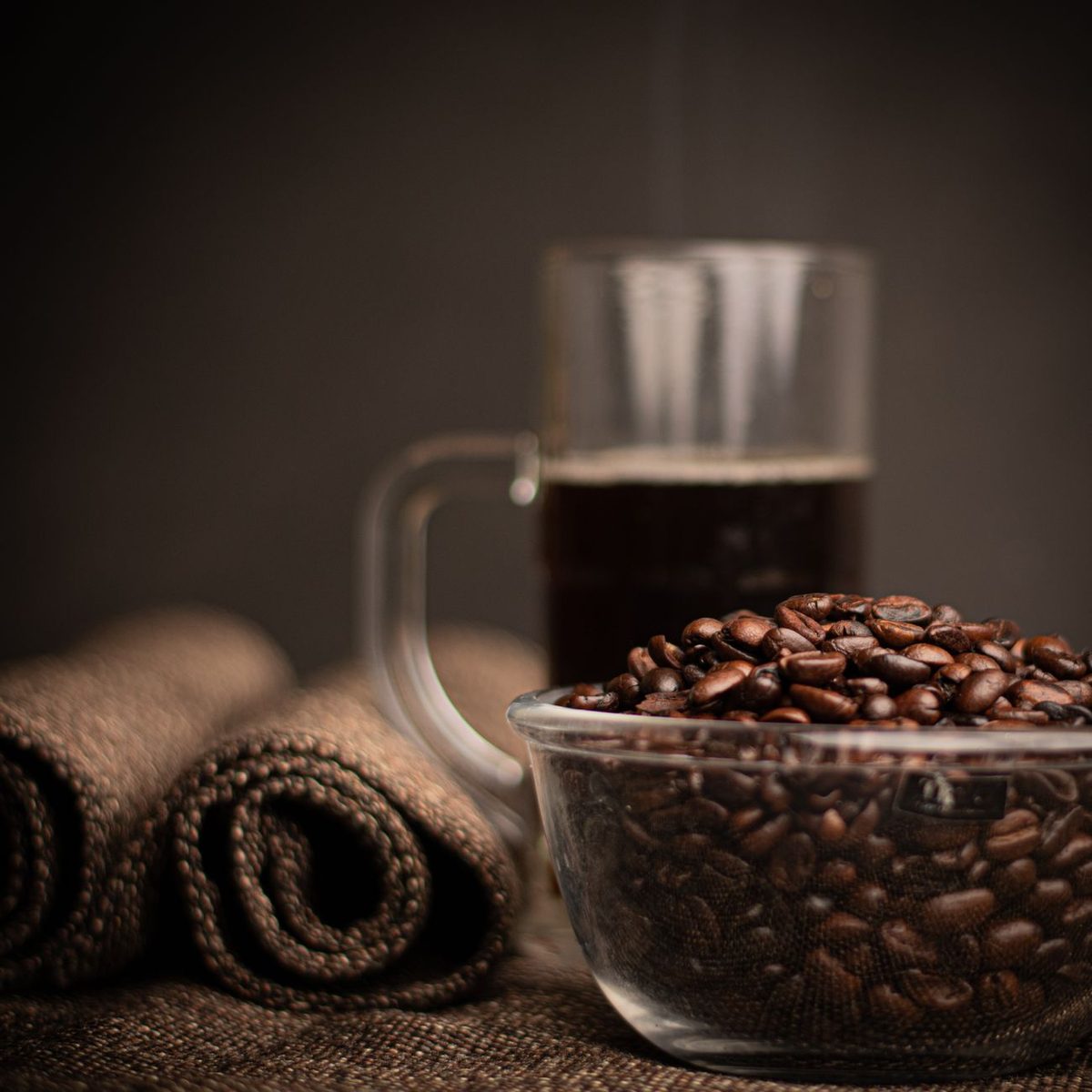 Granos de café tostado junto a una taza servida sobre la mesa