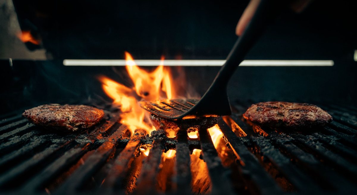 Tortas de carne dorándose al carbón mientras el parrillero las voltea