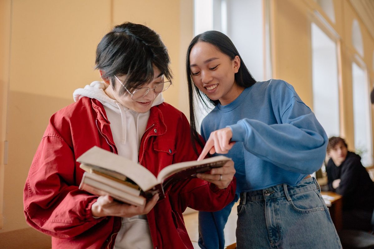 Dos adolescentes revisando un libro juntos en un pasillo con luz natural