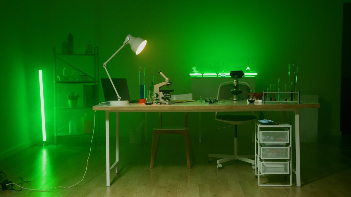 Laboratorio a oscuras iluminado por una luz verde, con mesas de trabajo y microscopios