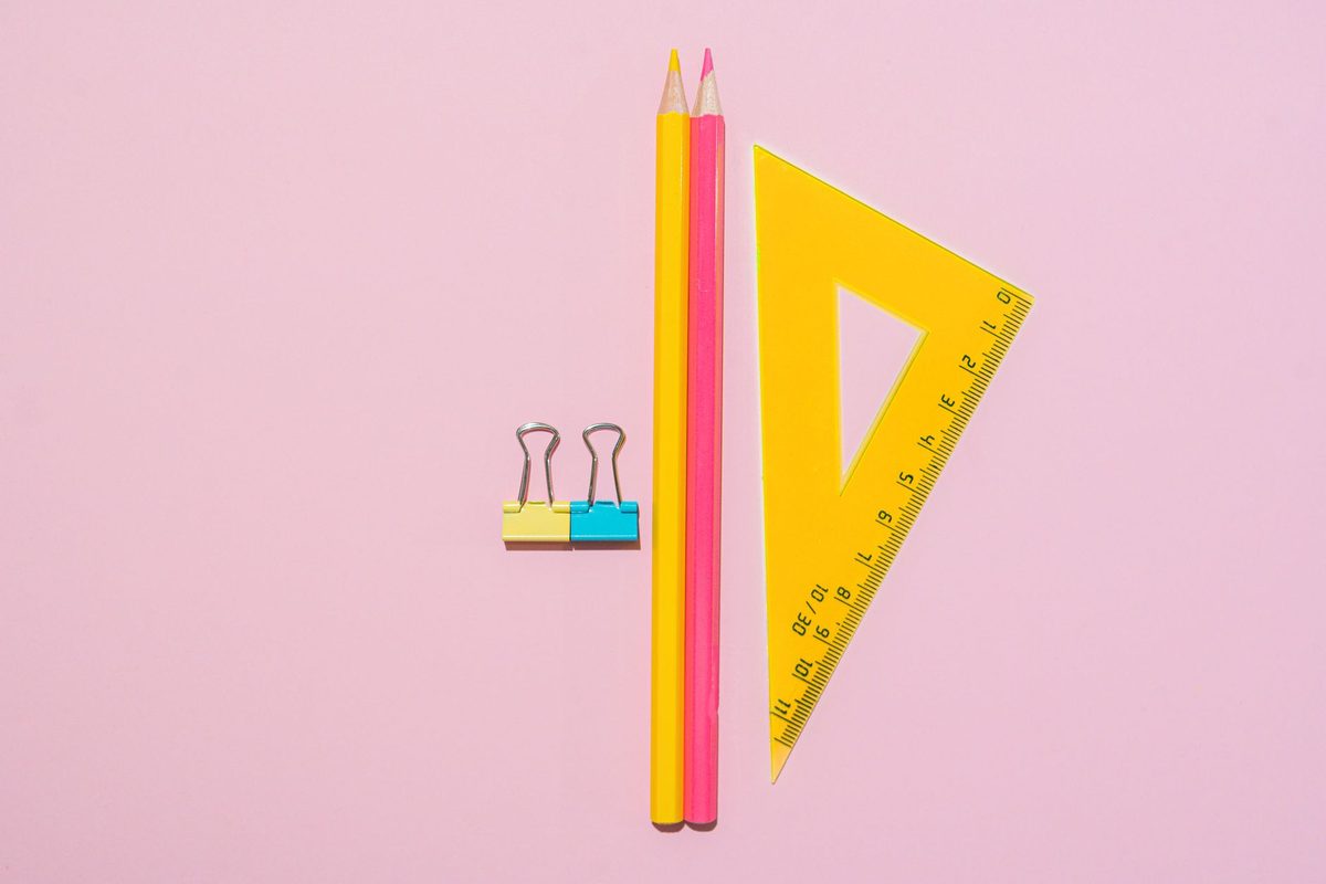 Lápices de colores y una escuadra sobre fondo rosado