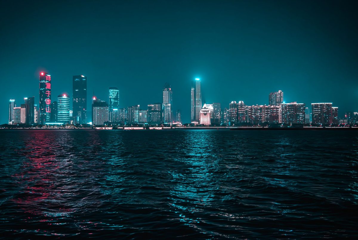 Ciudad de noche reflejada en el agua con luces cian