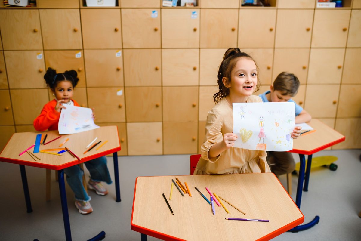 Niños en el aula mostrando sus dibujos sobre mesas rojas