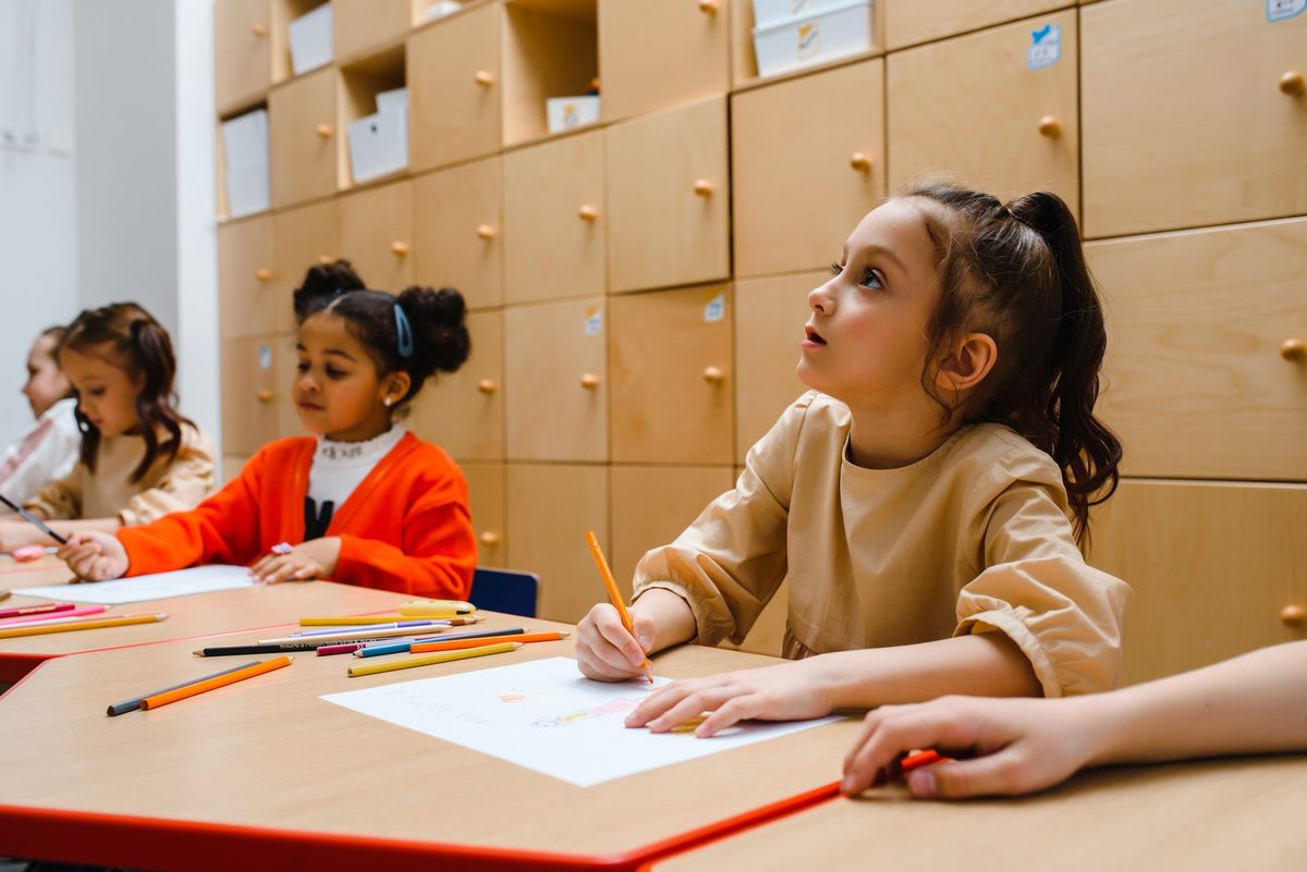 Niños y niñas dibujando en mesas de colores dentro de un aula luminosa